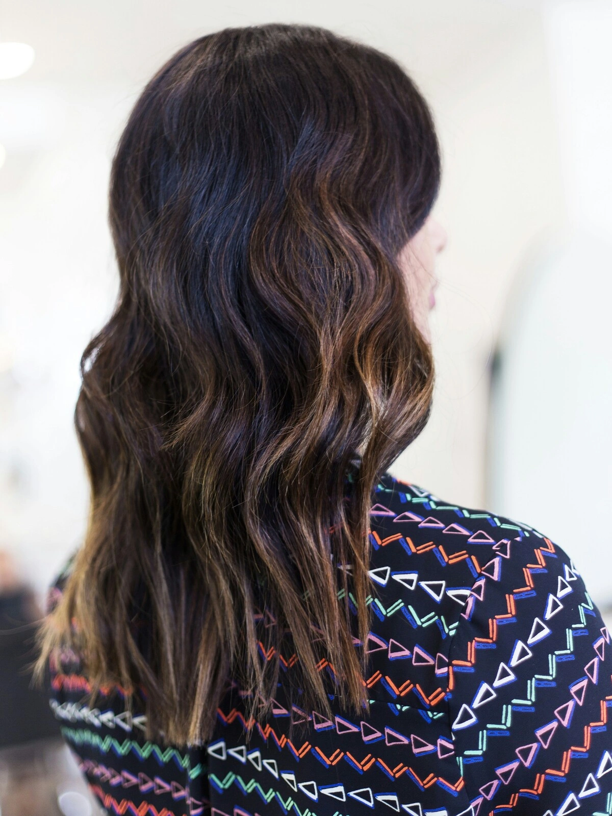 Vue de dos de la tête d'une femme montrant un balayage en vagues souples où les cheveux noirs se fondent dans des tons bruns chauds