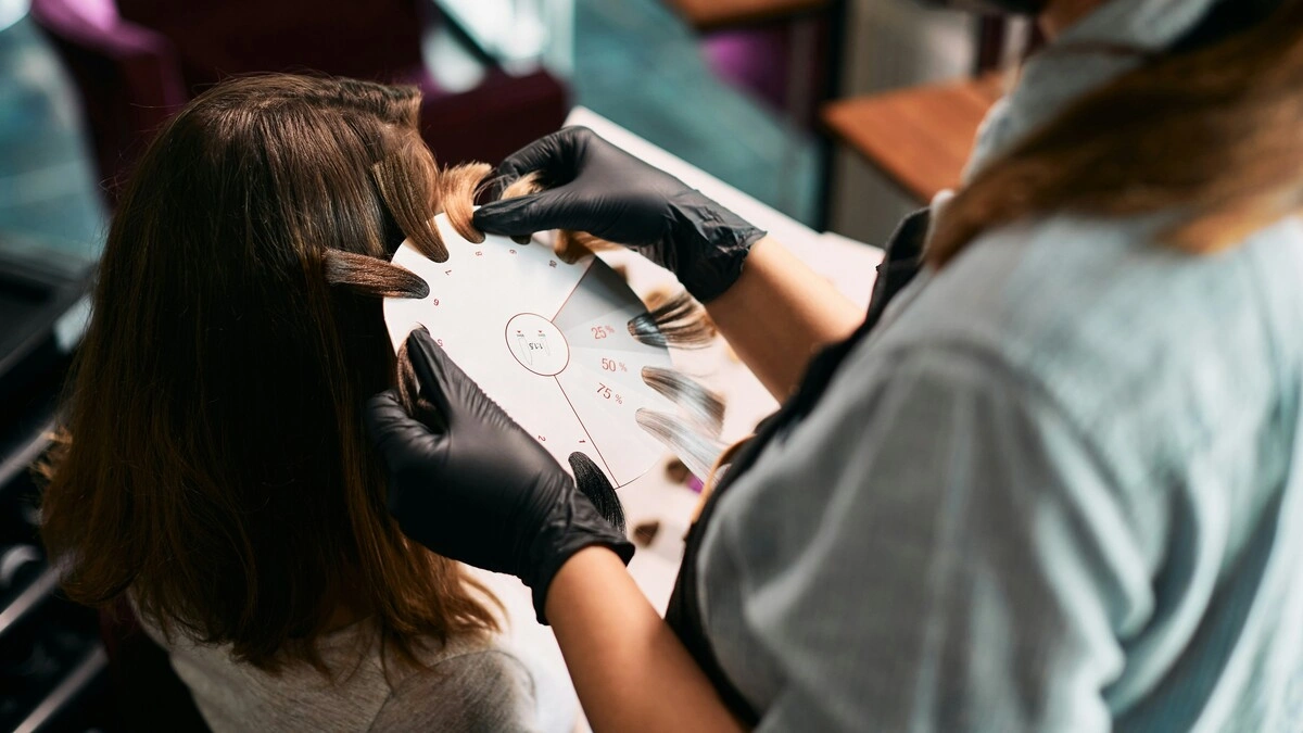 Gros plan d'une coloriste tenant des échantillons de mèches contre la tête d'une cliente pour choisir les nuances d'un balayage