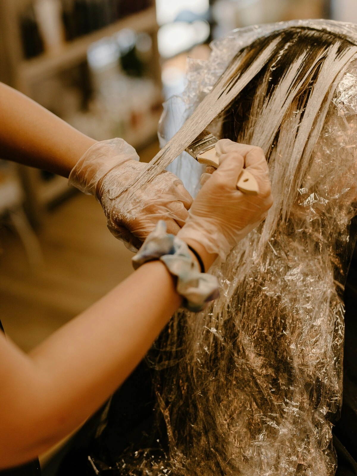 Une coloriste gantée applique de la couleur au pinceau sur les cheveux d'une cliente, dans le cadre d'un balayage
