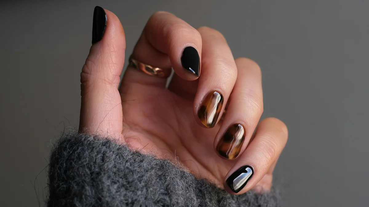 Gros plan d’une main aux ongles courts et à la manucure gel brillante, dans des tons noir et imprimé animal