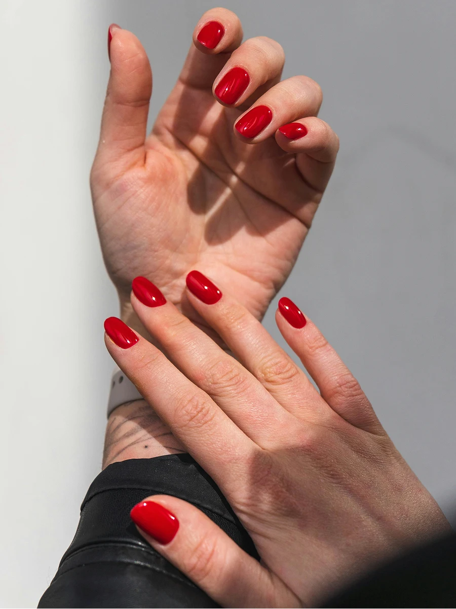 Gros plan des avant-bras d’une femme portant une veste en cuir noir et arborant une manucure gel rouge brillante
