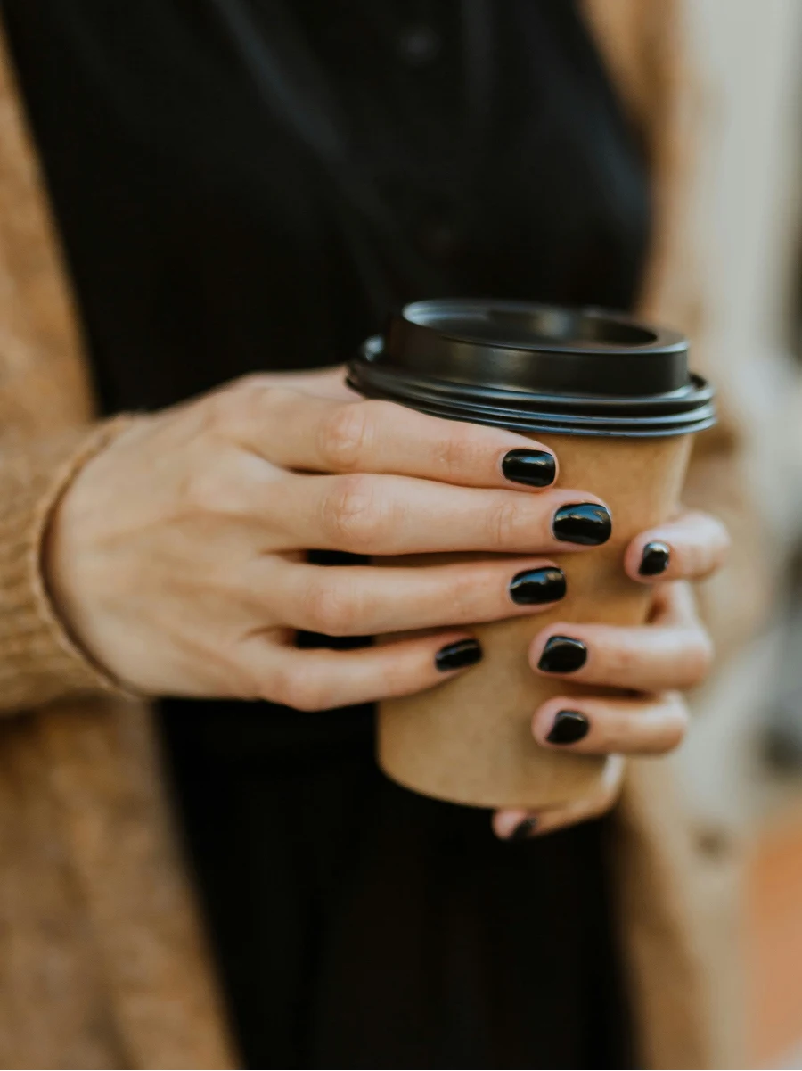 Gros plan d’une femme à la manucure gel noire brillante tenant un gobelet de café à emporter