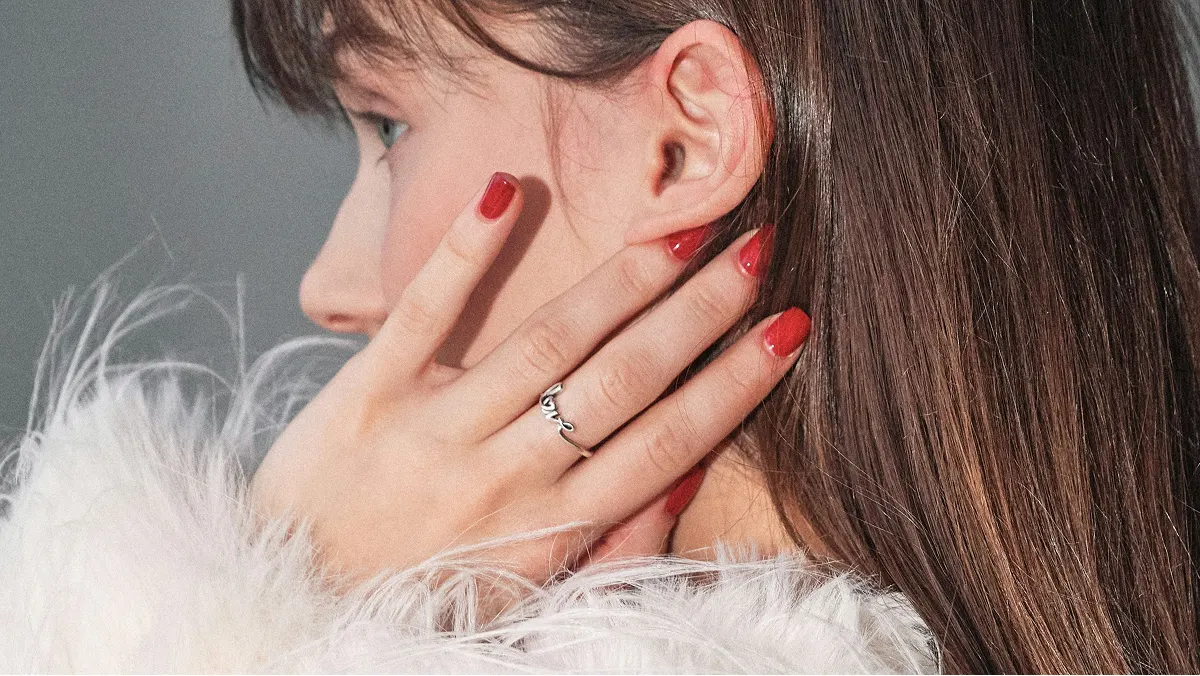 Vue de profil en gros plan de la tête d’une femme brune, sa main posée sur son visage révélant une manucure gel rouge brillante
