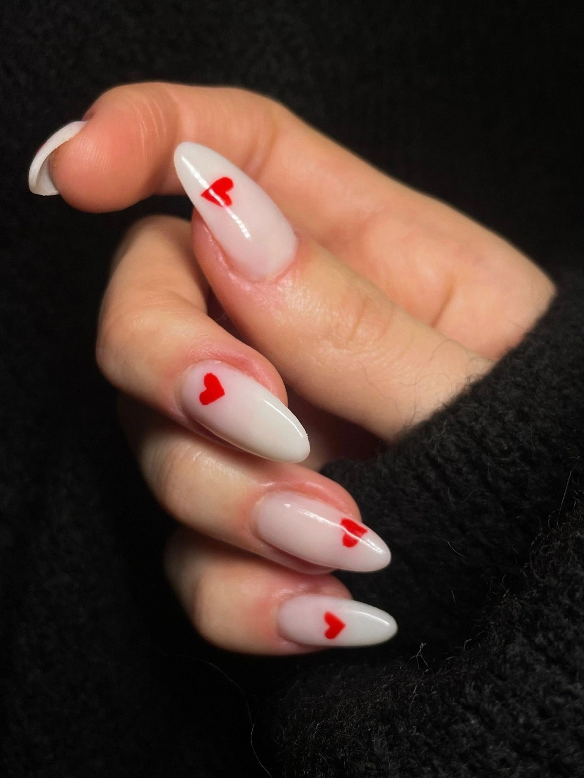 Gros plan sur la main d'une femme avec des ongles en résine blancs en forme d'amande, décorés de petits cœurs rouges
