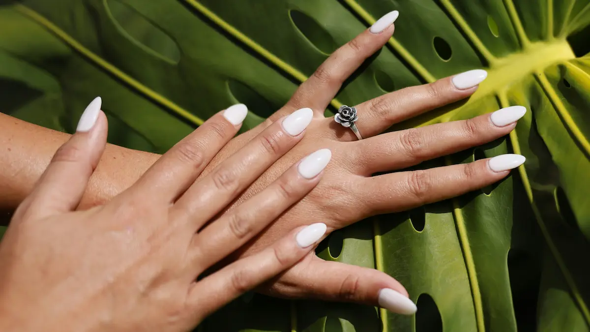 Photo studio d'ongles en résine fraîchement posés, forme amande et teinte nude, sur fond de feuille de palmier