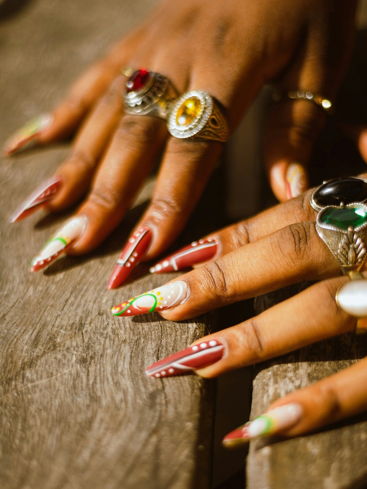 Gros plan sur les mains d'une femme avec des ongles en résine en forme de stiletto, rouges et blancs, décorés de points et de volutes vert et jaune