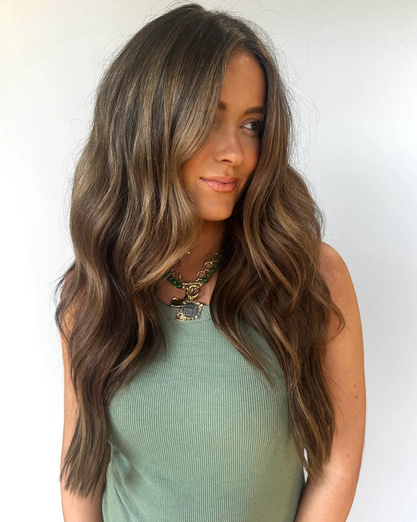 Longs cheveux bruns ondulés avec de douces mèches françaises ensoleillées concentrées sur les longueurs et les pointes