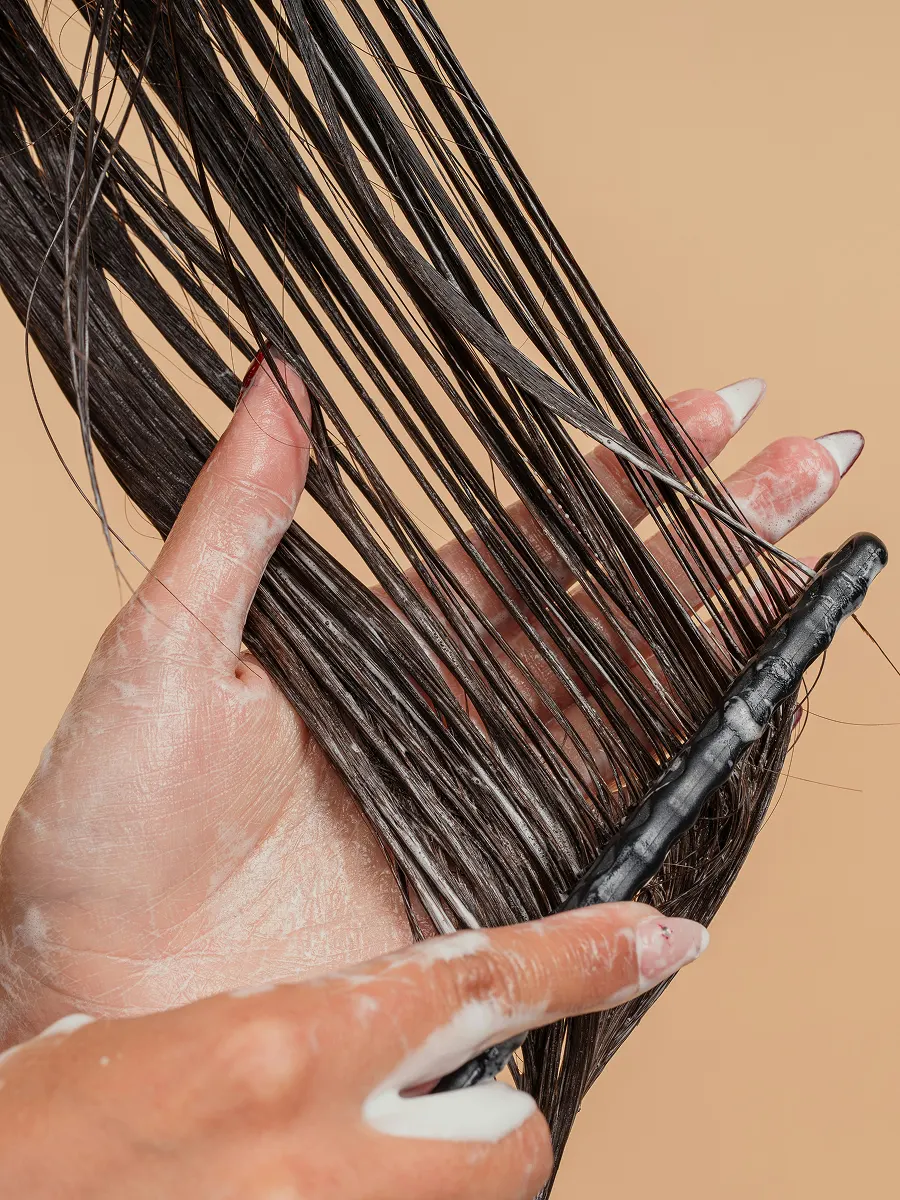 Gros plan d’une femme qui répartit de l’après-shampoing dans ses longs cheveux à l’aide d’un peigne à dents larges