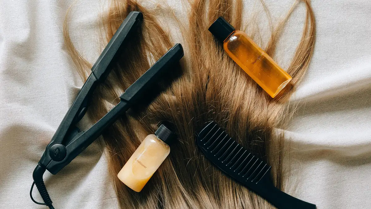 Mise à plat de produits capillaires disposés sur de longs cheveux raides : shampoing, après-shampoing, fer à lisser et peigne à dents larges