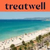 Vue aérienne de la Playa de Palma à Majorque : une longue courbe de sable doré, des rangées de parasols, une eau turquoise et calme, et une promenade bordée de palmiers longeant la ville, avec des collines au loin sous un ciel bleu limpide.