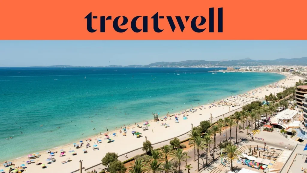 Vue aérienne de la Playa de Palma à Majorque : une longue courbe de sable doré, des rangées de parasols, une eau turquoise et calme, et une promenade bordée de palmiers longeant la ville, avec des collines au loin sous un ciel bleu limpide.