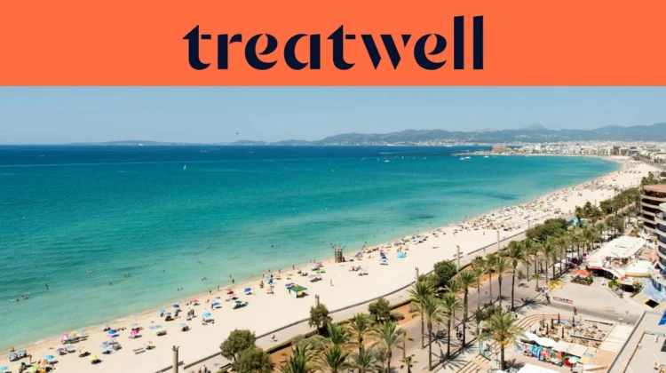 Vue aérienne de la Playa de Palma à Majorque : une longue courbe de sable doré, des rangées de parasols, une eau turquoise et calme, et une promenade bordée de palmiers longeant la ville, avec des collines au loin sous un ciel bleu limpide.