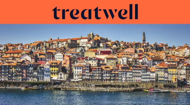 Les quais de la Ribeira à Porto, avec leurs rangées de maisons colorées et de toits en terracotta qui grimpent la colline depuis le Douro, et la tour des Clérigos à l'horizon sous un ciel bleu limpide.