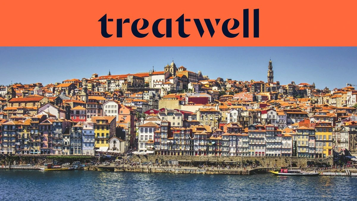 Les quais de la Ribeira à Porto, avec leurs rangées de maisons colorées et de toits en terracotta qui grimpent la colline depuis le Douro, et la tour des Clérigos à l'horizon sous un ciel bleu limpide.