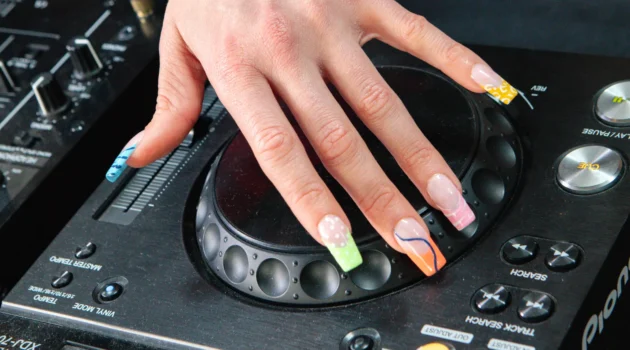 Une main arborant l’electric mani posée sur le jog wheel d’une platine DJ Pioneer, avec des french tips fluo en imprimé animalier et en volutes