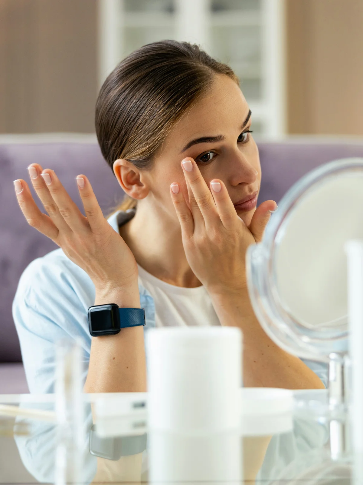 Une femme assise à une table applique délicatement une crème hydratante et des huiles sur son visage et ses sourcils