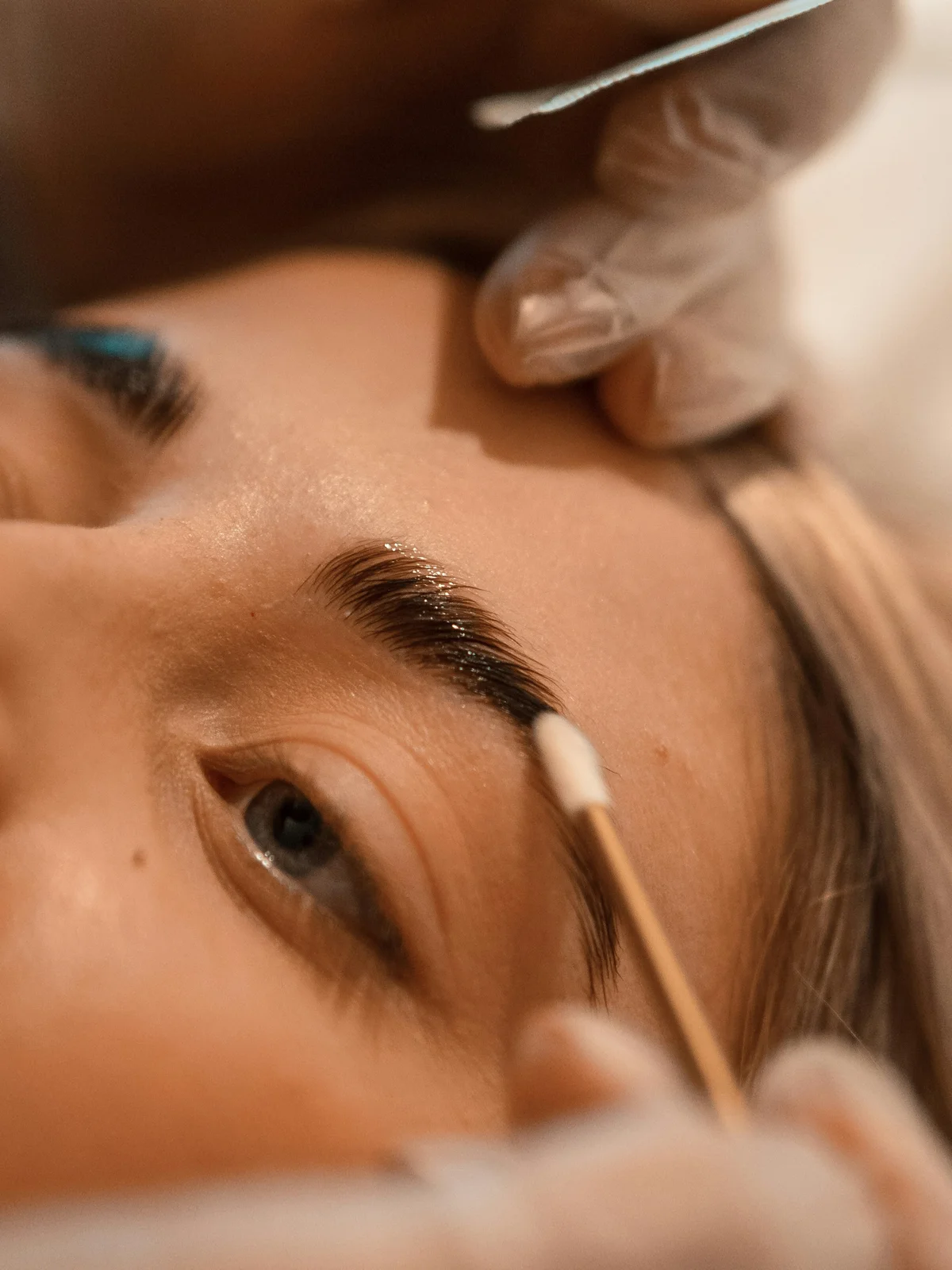 Gros plan d'une cliente allongée pendant qu'une esthéticienne réalise un soin de lamination des sourcils