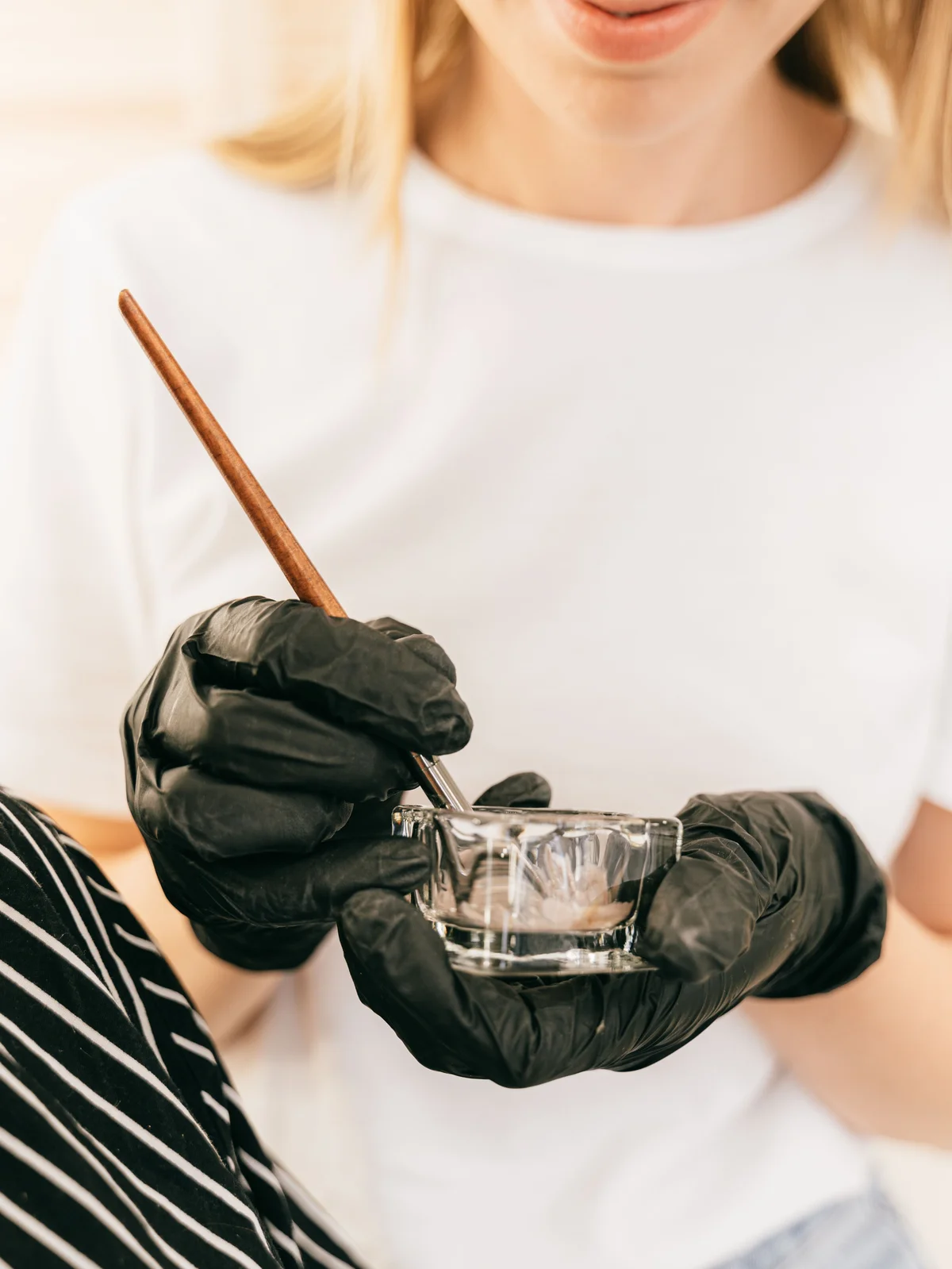Gros plan d'une esthéticienne tenant un petit pot en verre et un pinceau fin, mélangeant une teinture pour sourcils en institut