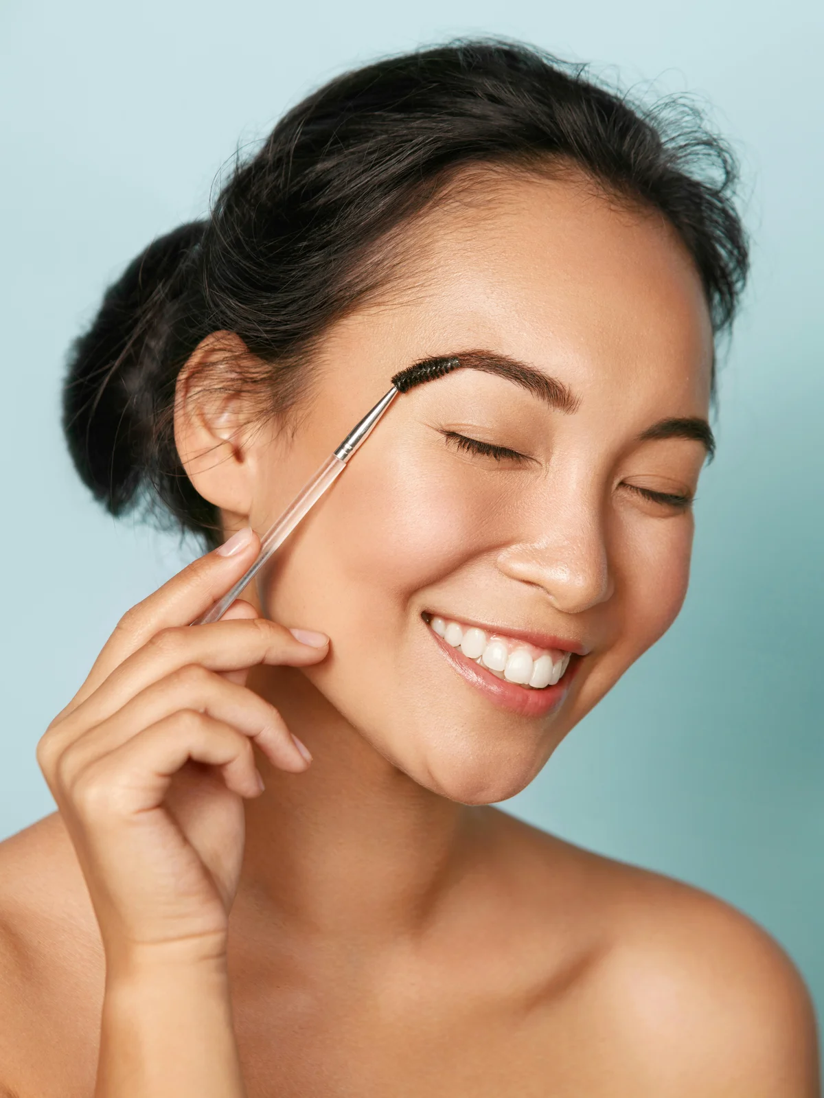 Photo studio d'une femme aux cheveux relevés, souriante, qui discipline ses sourcils avec un goupillon