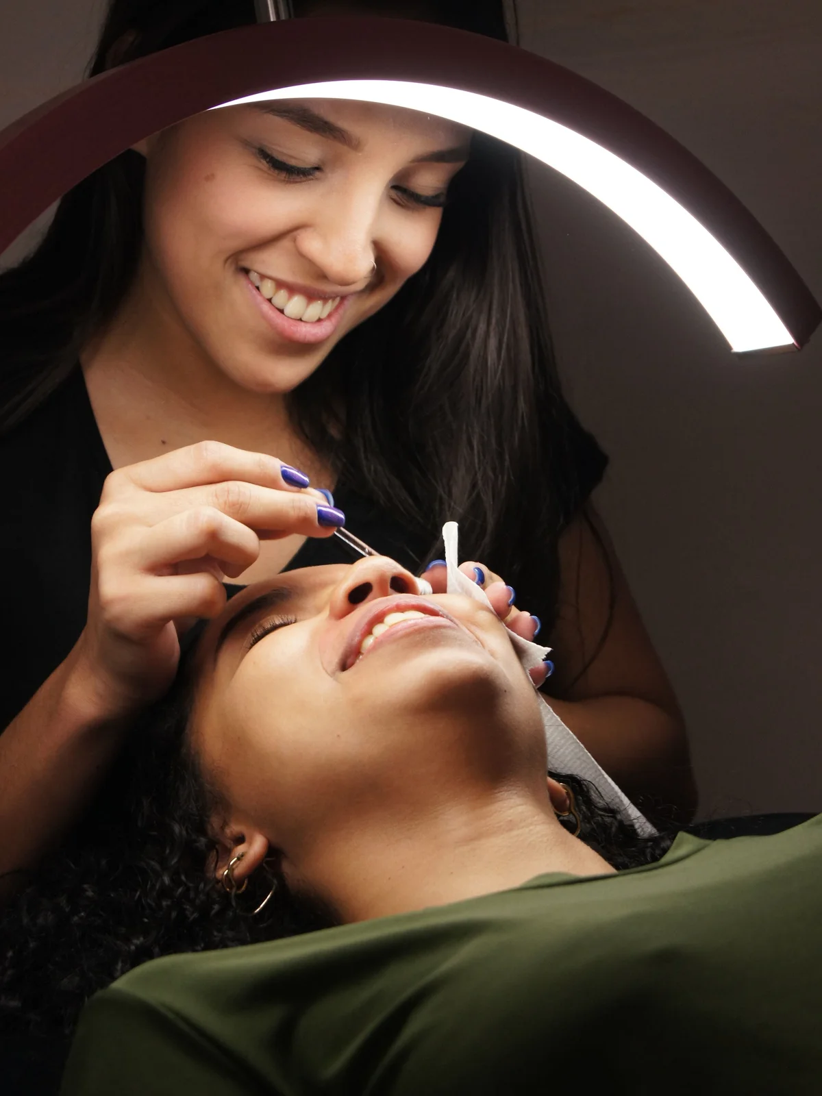 Gros plan d'une esthéticienne appliquant une teinture sur les sourcils d'une cliente allongée et détendue sur la table de soin, en institut