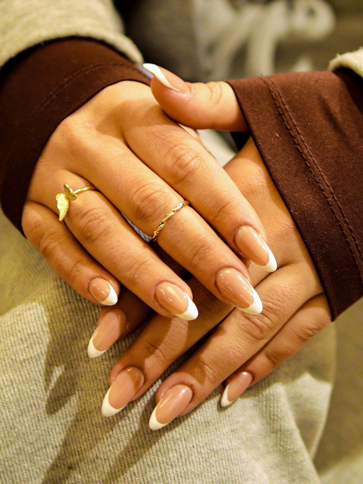 Les mains d'une femme arborant une French manucure audacieuse dans une association de beige et de blanc sur de longs ongles en amande
