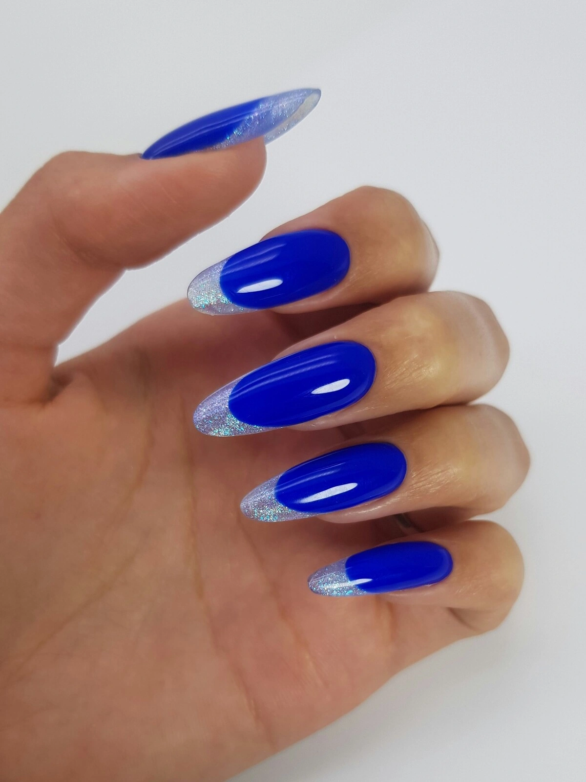 La main d'une femme arborant une French manucure audacieuse avec une base bleu vif et des pointes métallisées argentées sur de longs ongles en amande