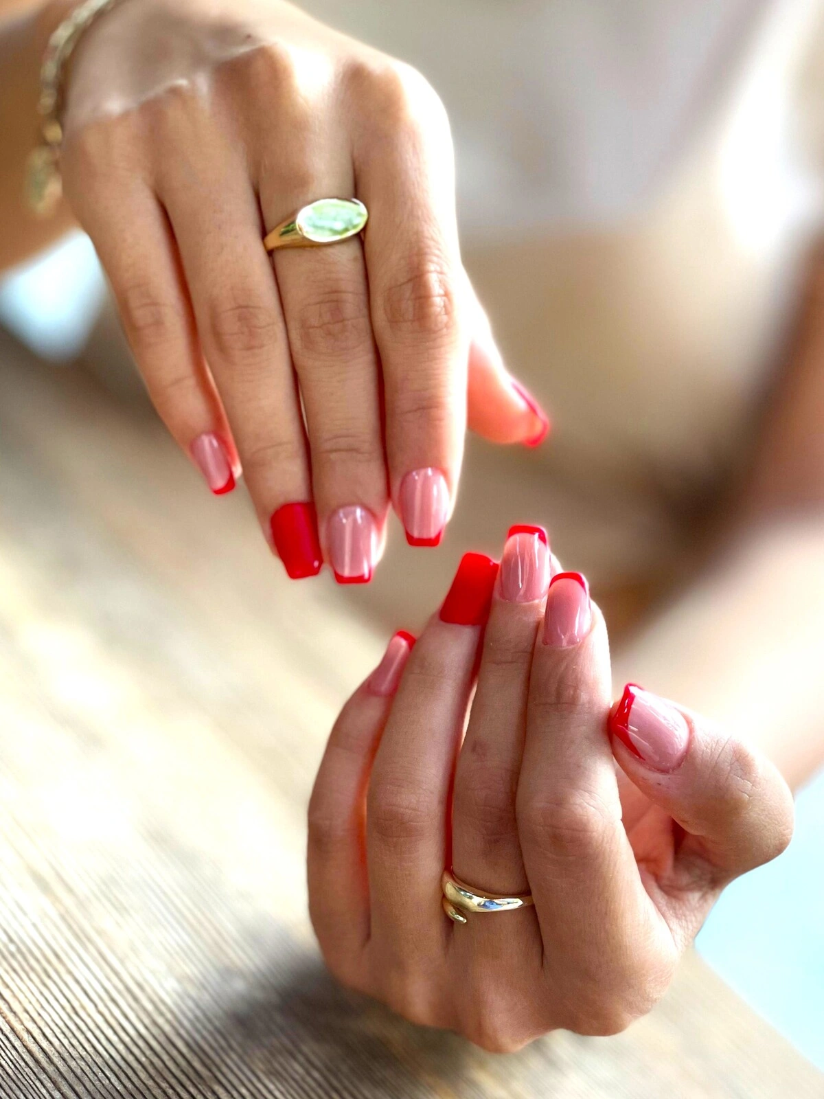 Une French manucure sur des ongles carrés-ovales avec une base rose pâle et des pointes rouges, et des annulaires entièrement rouges