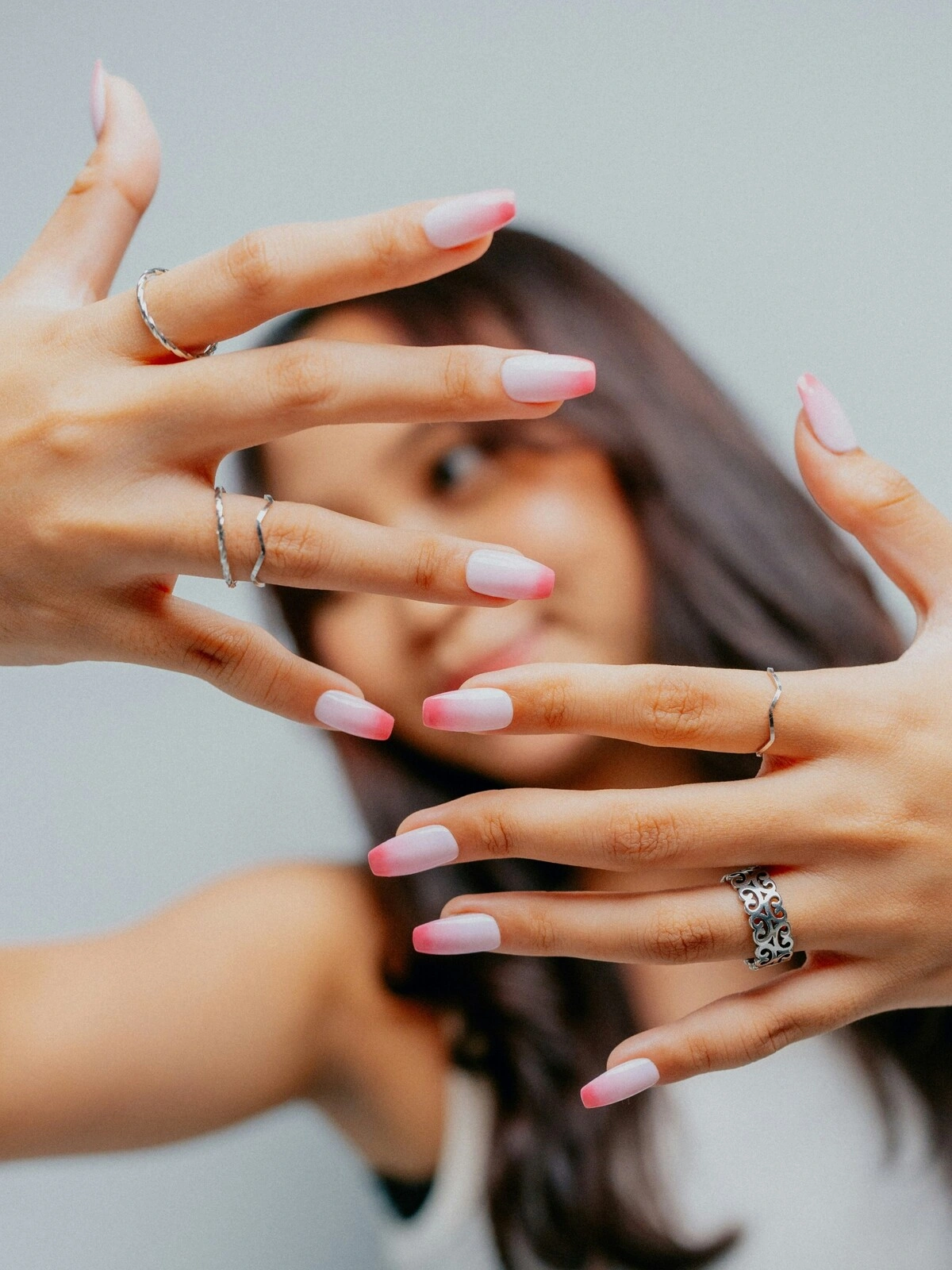 Une femme présente ses mains à l'objectif, arborant une French manucure ombrée avec une base rose pâle et des pointes rose vif sur des ongles ballerine