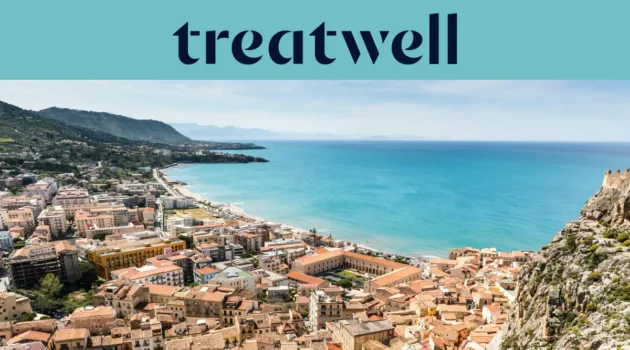 Vue panoramique sur une petite ville côtière sicilienne, avec de vieux bâtiments aux toits de terre cuite, un croissant de plage de sable, une mer turquoise limpide et un promontoire rocheux qui s'élève sur un côté.