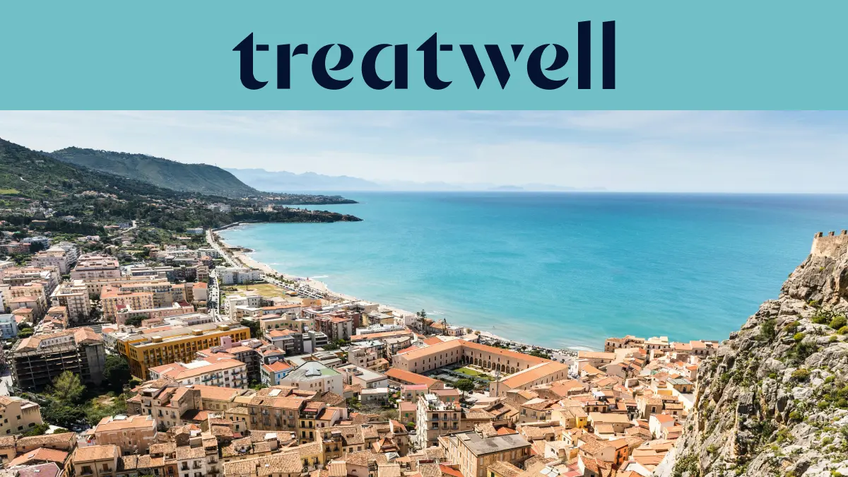 Vue panoramique sur une petite ville côtière sicilienne, avec de vieux bâtiments aux toits de terre cuite, un croissant de plage de sable, une mer turquoise limpide et un promontoire rocheux qui s'élève sur un côté.