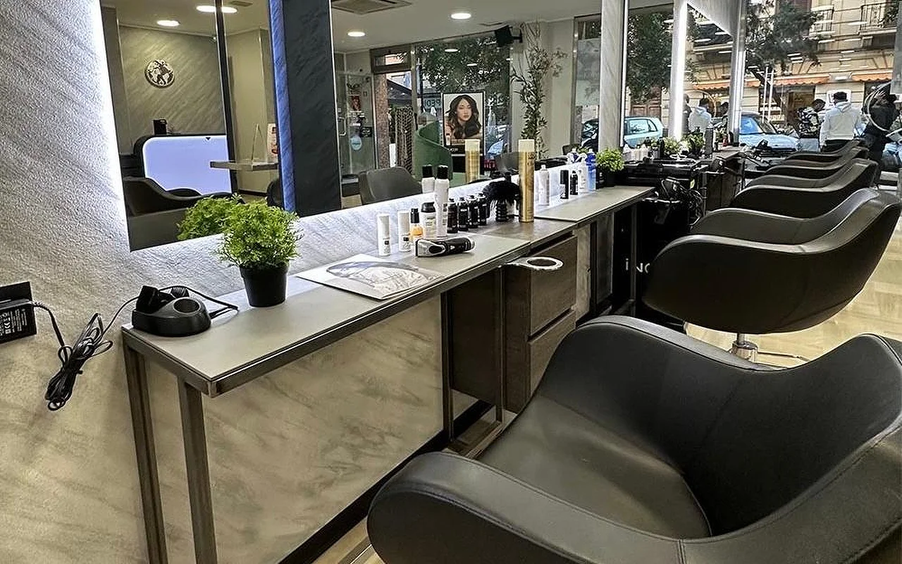 L'espace coiffage d'Equipe Beauty, avec une rangée de fauteuils noirs le long d'un comptoir effet marbre, un grand miroir rétroéclairé, des produits de coiffage et une plante en pot sur le comptoir, et des baies vitrées du sol au plafond donnant sur la rue.