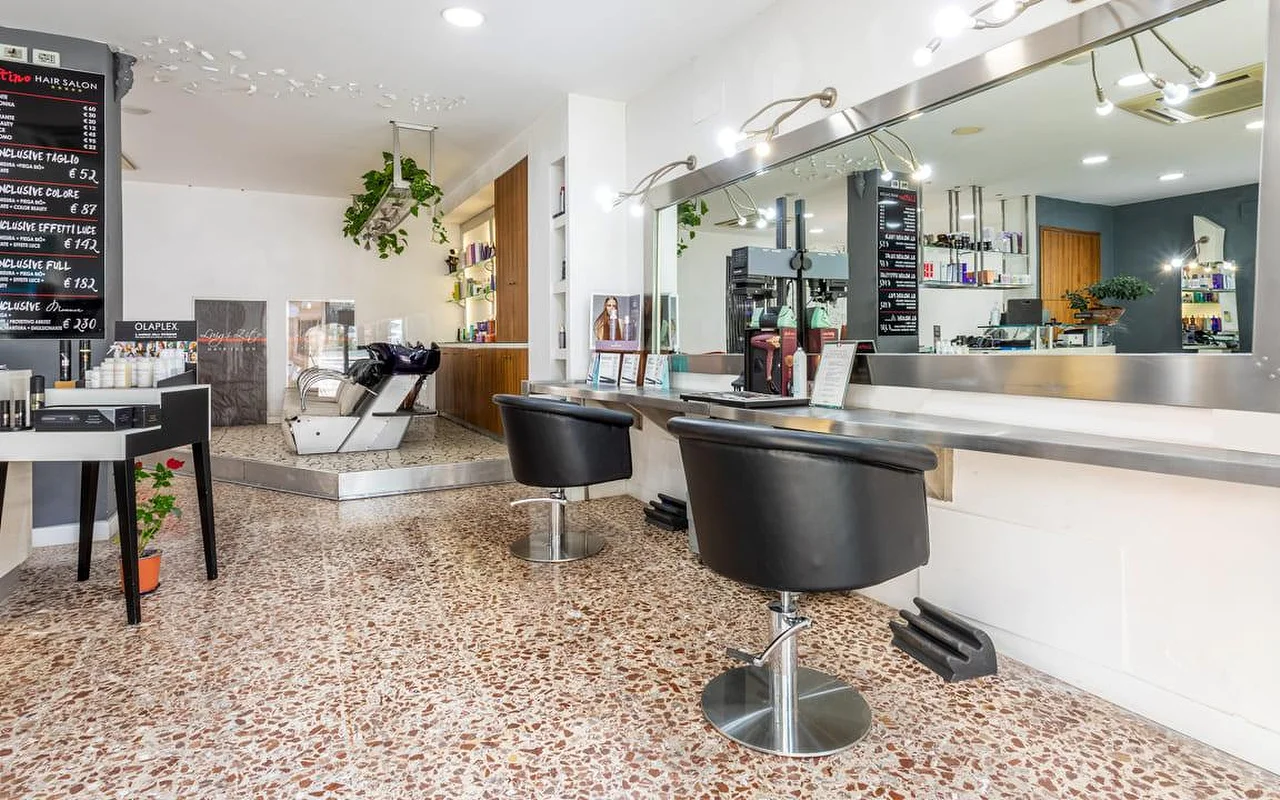 L'intérieur du Hair Salon Luigi Zito, avec un sol en terrazzo, deux fauteuils de coiffage noirs face à un long miroir, des tarifs à la craie au mur, un présentoir de produits et un bac de lavage à l'arrière-plan.