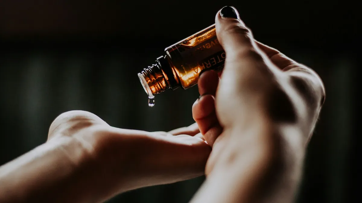 Gros plan sur les mains d'une praticienne versant quelques gouttes d'huile d'un flacon en verre dans la paume de son autre main